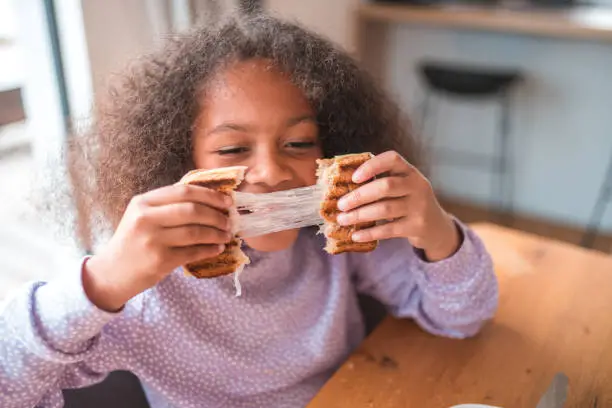 Photo of Cute And Playful Girl Eating A Cheese Sandwich