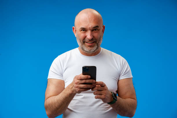 istock Happy middle-aged man with a phone in his hands against blue background 1403363270