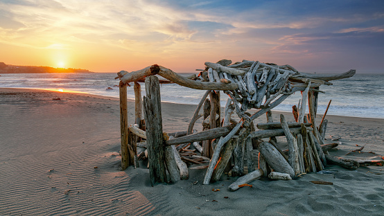 Driftwood hut, fort or house on beach with sunset by ocean