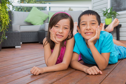 Smiling mixed raced young sibling portrait laying on brown wooden patio deck.