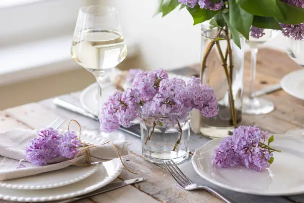 Beautiful table decor for a wedding dinner with a spring blooming lilac flowers. Celebration of a special event. Fancy white plates, wineglasses. Countryside style