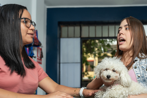 Latina woman holding a dog while talking with a pet salon receptionist talking in the counter