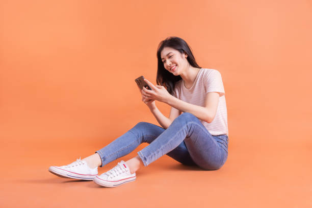istock Full length image of young Asian girl using smartphone on orange background 1403384355