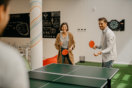 Group of young startup business people playing table tennis together on a boardroom table in an office game room while taking a break from their meeting. Work and fun concept