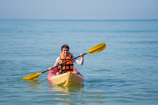 man in life jacket paddling a kayak boat in the sea