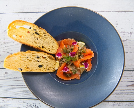 Portion of cold smoked salmon with roasted capers and bread.