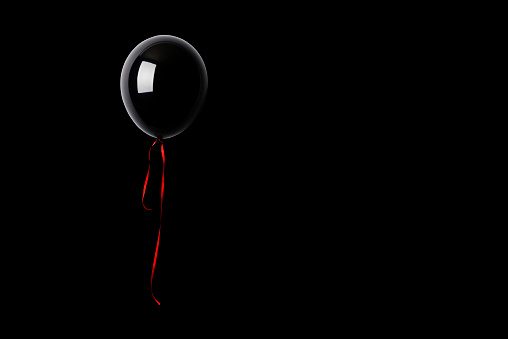 Black balloon floating in mid-air against black background with copy space.