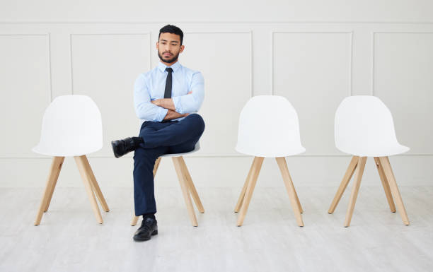 larga duración de un empresario asiático esperando una entrevista. un joven solicitante impaciente sentado solo. profesional étnico con los brazos cruzados en la fila para la oferta de trabajo, la vacante y la oportunidad en el cargo - con las piernas cruzadas fotografías e imágenes de stock