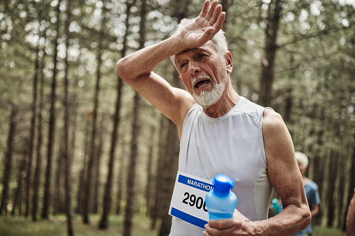 Mature male runner feeling tired after the marathon in the forest. Copy space.