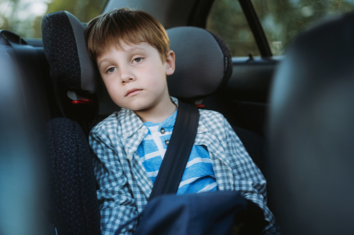 Little boy feeling sick travelling by car sitting in child seat fastened with belt. Image with selective focus