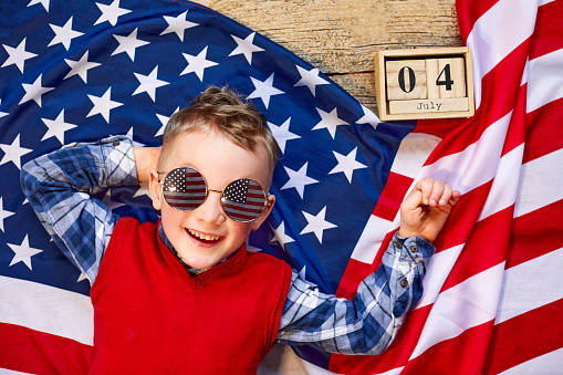 Cute and cheerful guy lying on a wooden background next to the American flag with glasses