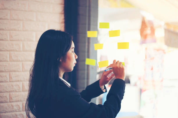 istock businesswoman write tasks creative ideas and planning on sticky post it note on glass wall. 1403398006