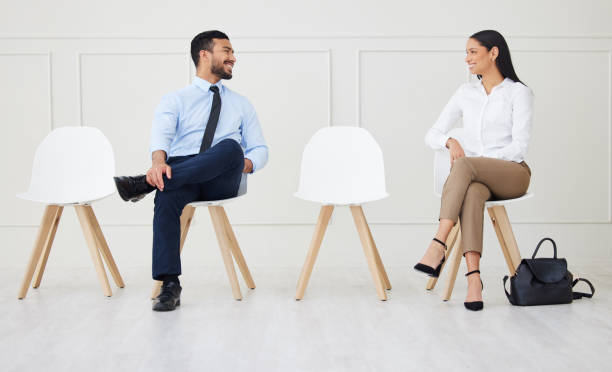 dos empresarios hablando mientras esperan la entrevista. sonriente hombre de negocios asiático y empresaria mestiza manteniendo la distancia social. candidato en línea para la oferta de trabajo, vacante, oportunidad de oficina - con las piernas cruzadas fotografías e imágenes de stock