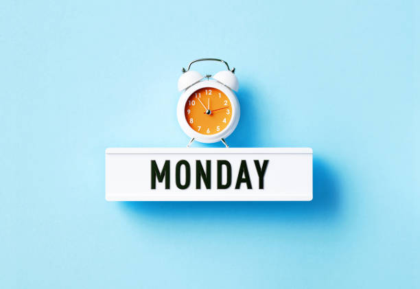 Alarm clock sitting above Monday written white lightbox on blue background. Horizontal composition with copy space.
