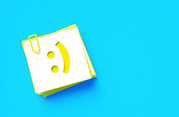 Cut Out Yellow Adhesive Note With Happy Face Symbol Sitting Over Blue Background Cut out yellow adhesive note with happy face symbol sitting on blue background. Horizontal composition with copy space. smiley face postit stock pictures, royalty-free photos & images