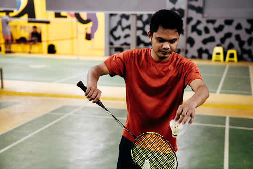 Mid adult man hitting shuttlecock with badminton racquet in court.