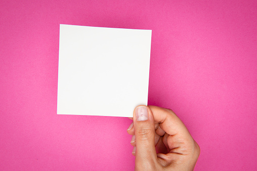 Woman holding greeting card in front of a pink background.