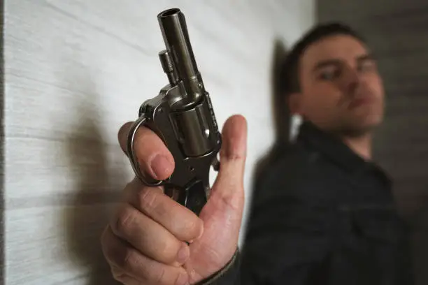Photo of Threat to life. Close-up of hand with pistol. Shootout of criminals with revolvers. Killer or murderer. bandit hides in the dark with a firearm. shooter is in ambush