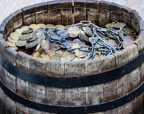 A lot of coins and chain in a wooden barrel