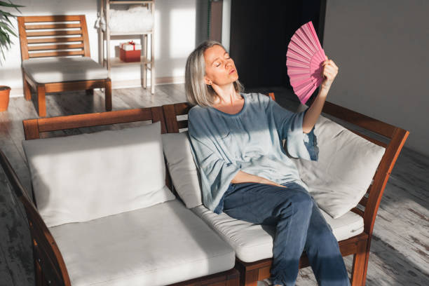 istock Exhausted middle aged woman using paper waver, suffering from hot summer 1403408591