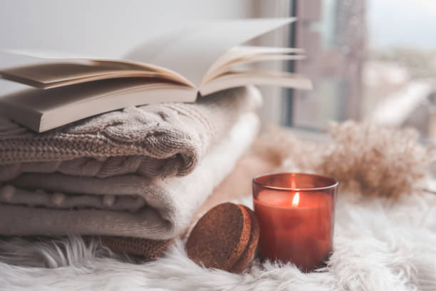 istock Burning candle and sweaters with a book on the windowsill. Autumn mood. 1403411229