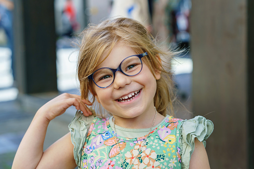 Portrait of a cute preschool girl with eye glasses outdoors. Happy funny child wearing new blue glasses