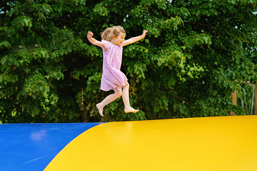 Little preschool girl jumping on trampoline. Happy funny toddler child having fun with outdoor activity in summer. Sports and exercises for children. Trampolin in ukrainian flagg colors.