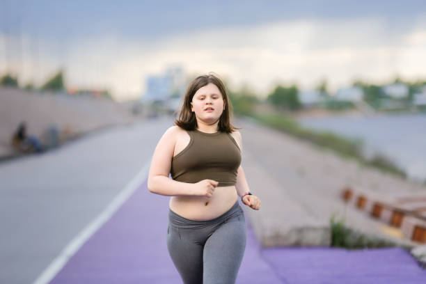 유럽의 십대 소녀 과체중 도시의 제방을 따라 디딜 방아에 조깅, 과체중 및 십대의 활동적인 생활 방식 - teen obesity 뉴스 사진 이미지