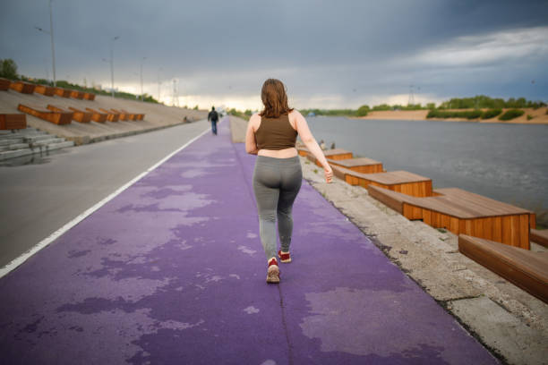 europäisches teenager-mädchen übergewichtig beim joggen auf dem laufband entlang der böschung der stadt, übergewichtig und aktiver lebensstil des teenagers - teen obesity stock-fotos und bilder