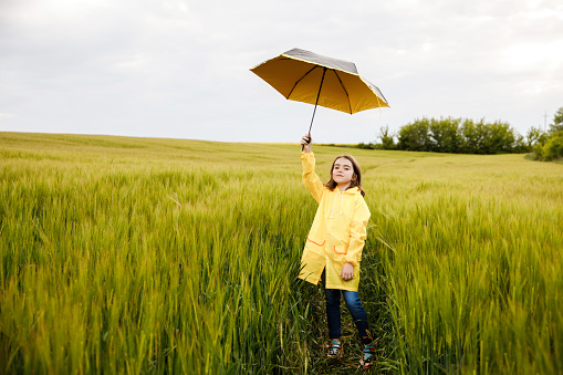 Pretty brunette girl standing in a field with an yellow umbrella in her hands