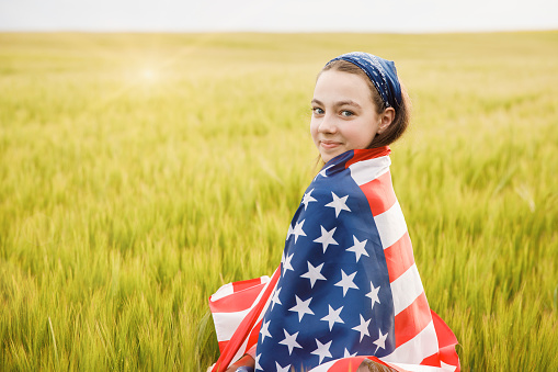Beautiful young smiling woman with American flag in a wheat field