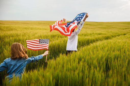 Guy and girl running in a field with an American flag in their hands. . Independence Day