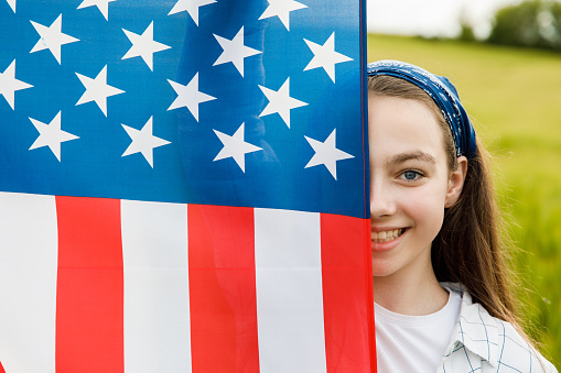 Pretty young pre-teen girl in field holding American flag. Independence Day