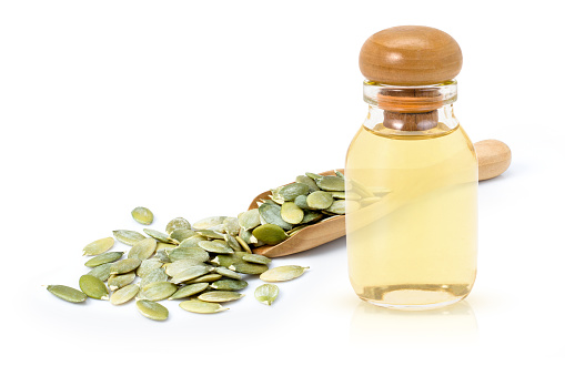 Pumpkin seed oil in glass bottle and dried pumpkinseed in wooden scoop isolated on white  background.