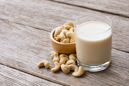 Glass of cashew milk and cashew nuts isolated on wooden table background.