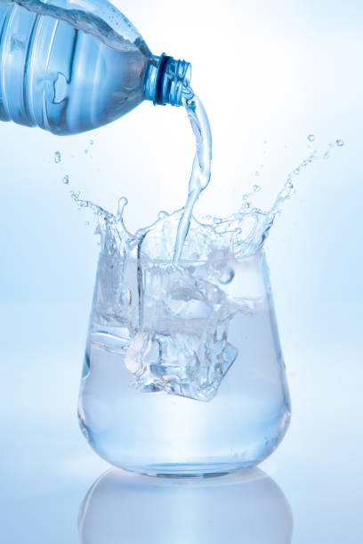 istock Pouring mineral water and splashing from bottle into glass on blue background. Vertical format. 1403420888