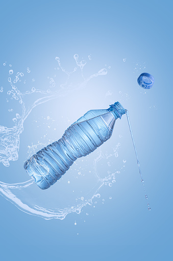 Flying bottle of mineral water with splash on blue background with copyspace and vertical format. Pure water levitation concept.
