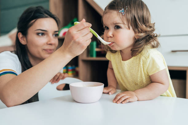 Mother feeding her girl Young mother feeding her baby girl with a spoon at home baby spoon stock pictures, royalty-free photos & images