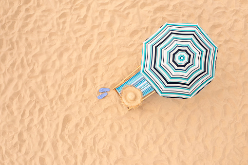 Striped beach umbrella near sunbed with vacationist's stuff on sandy coast, aerial view. Space for text