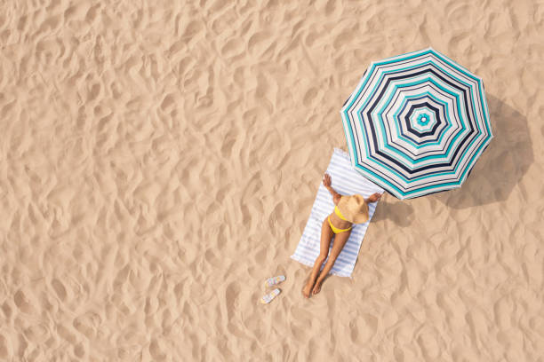 donna che riposa sotto l'ombrellone a strisce sulla costa sabbiosa, vista aerea. spazio per il testo - parasol umbrella sun beach foto e immagini stock