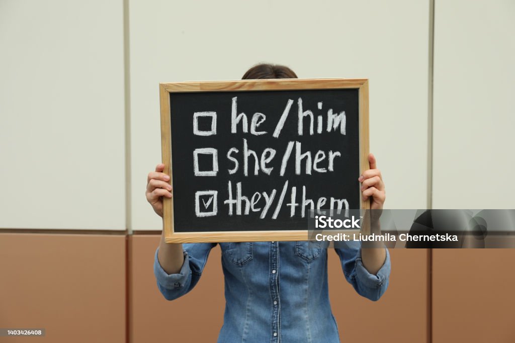 Woman holding chalkboard with list of gender pronouns near color wall Pronoun Stock Photo