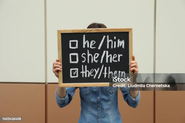 Woman Holding Chalkboard With List Of Gender Pronouns Near Color Wall Stock Photo - Download Image Now