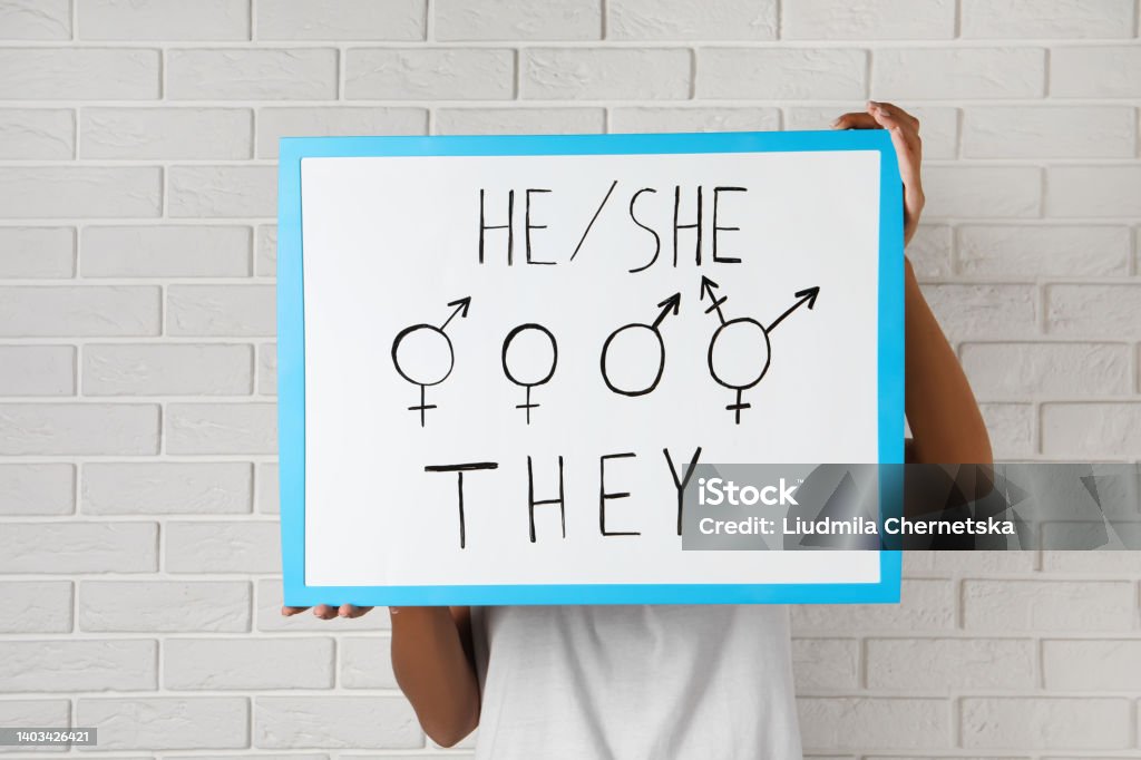 Woman holding sign with gender pronouns and symbols near white brick wall Pronoun Stock Photo