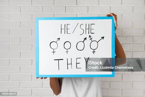 Woman Holding Sign With Gender Pronouns And Symbols Near White Brick Wall Stock Photo - Download Image Now