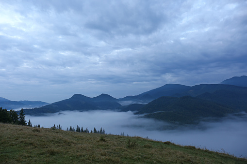 Picturesque view of mountains covered with fog under cloudy sky