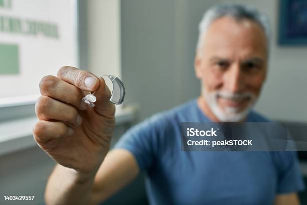 Senior Man Holding Bte Hearing Aid In Hand On Foreground Closeup Treatment Of Deafness In Elderly People Stock Photo - Download Image Now