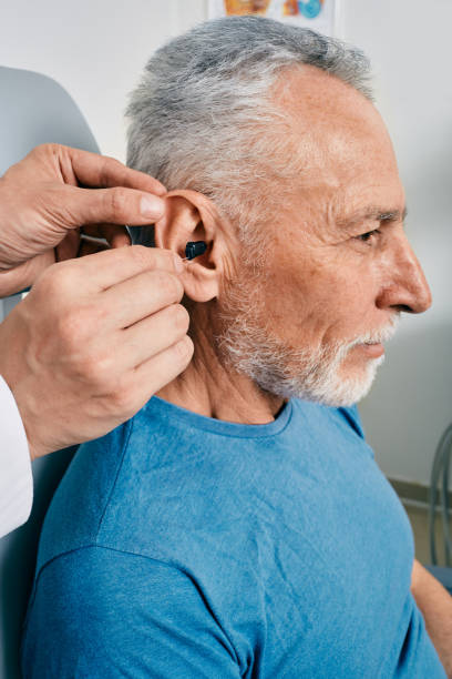 istock Senior man while installation hearing aid into his ear by his audiologist, close-up. Hearing treatment for hearing impaired people 1403429561