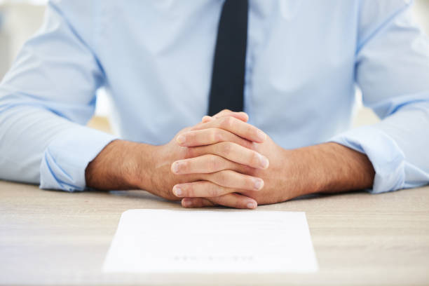 Unrecognizable businessman conducts a job interview with an unrecognizable female candidate. He is holding the woman's resume. The woman is sitting across the desk from him.
