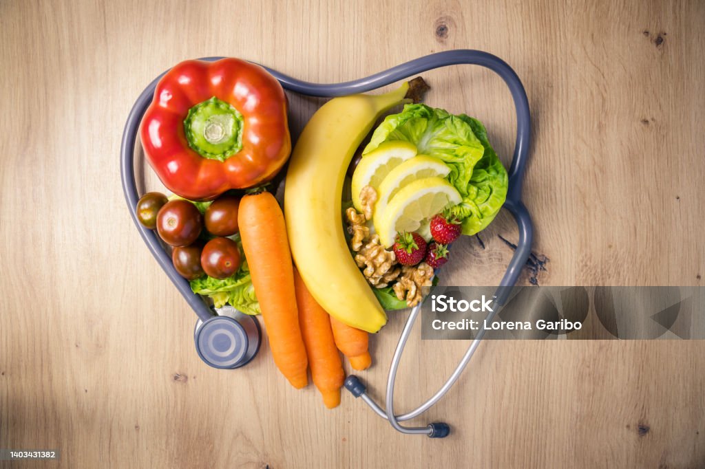 phonendoscope or stethoscope in the shape of a heart with fruits, vegetables and nuts in the center forming a heart on a wooden background phonendoscope or stethoscope in the shape of a heart with fruits, vegetables and nuts in the center forming a heart on a wooden background, bell pepper, carrot, banana, strawberries Food Stock Photo