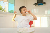 自宅でマシュマロとキッチンに座ってかわいい面白いアジアの男の子、不健康な子供のおやつ